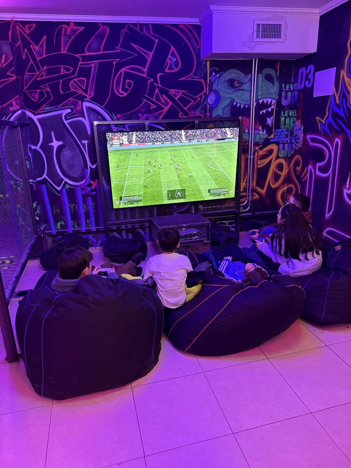 Chicos en pufs mirando el FIFA en la pantalla grande
